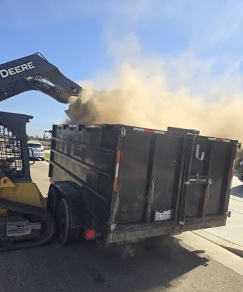 A dump truck is dumping dirt into a truck bed