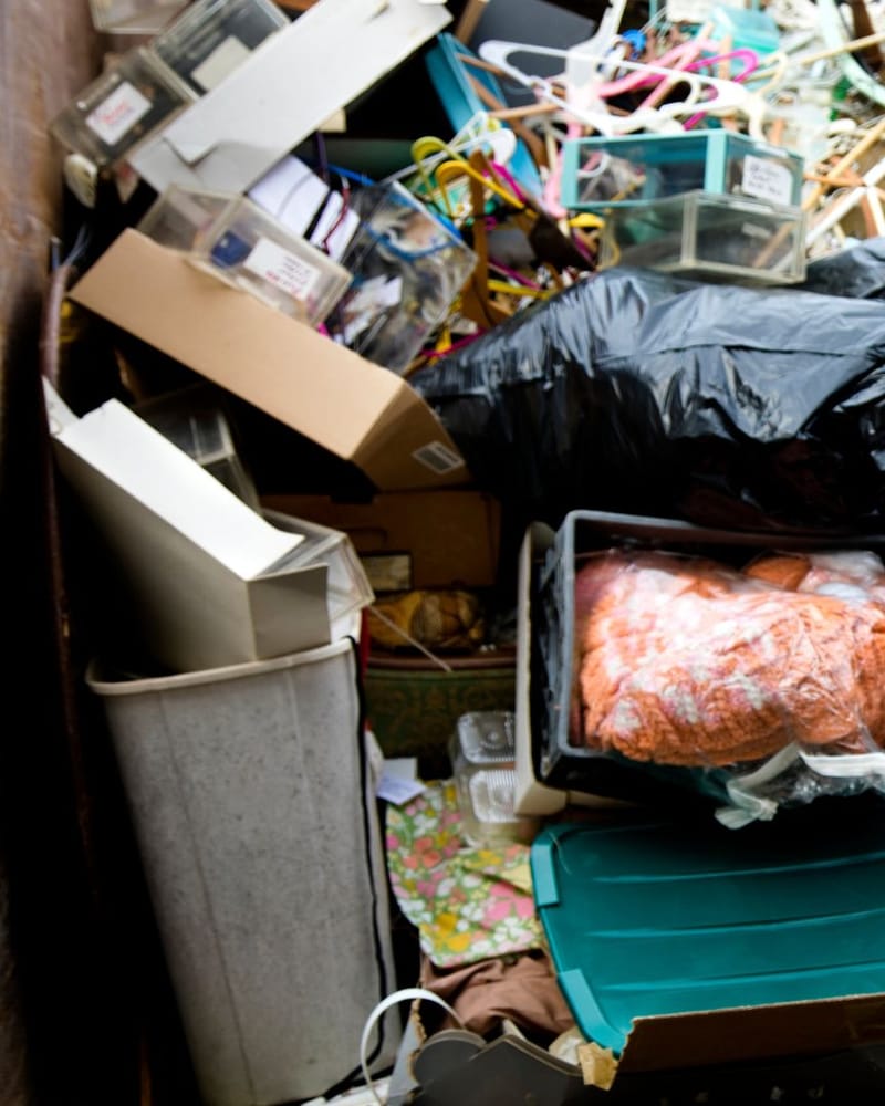 Gloved worker carefully bagging and removing accumulated household items during a cleanup