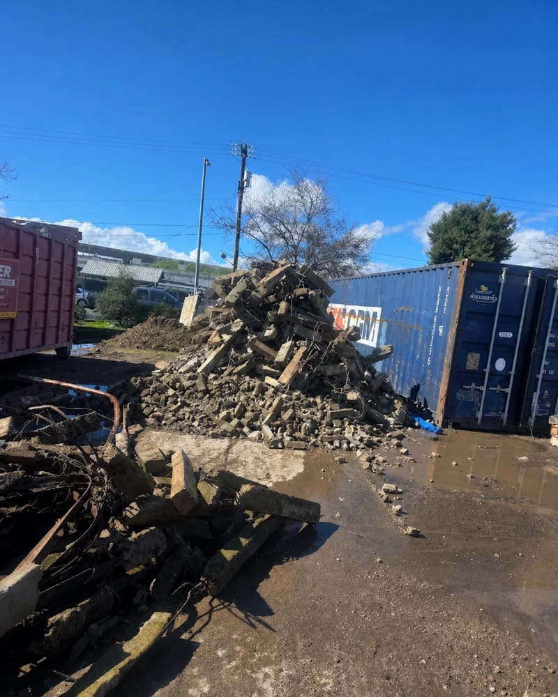Broken concrete and demolition rubble stacked beside a shipping container on a Fresno job site