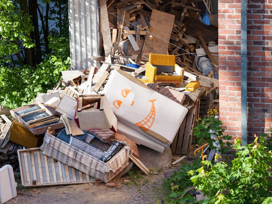 Yard debris and cleared brush stacked beside a shed awaiting collection