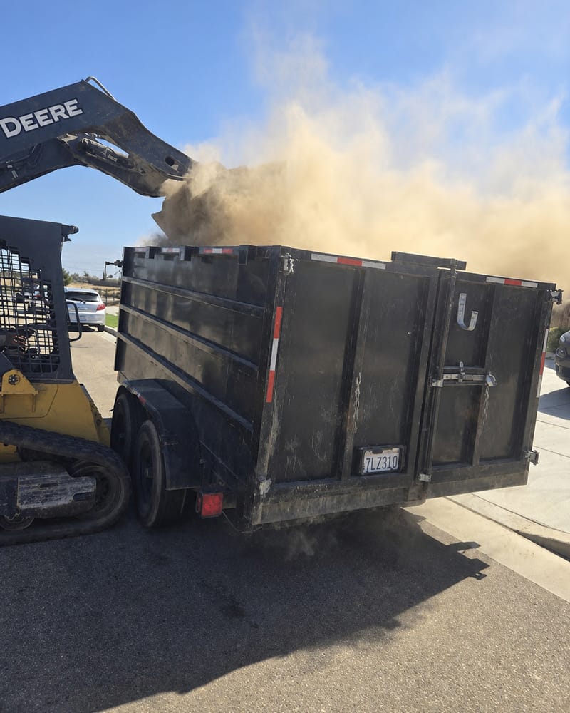 Skid steer loading soil and demolition spoil into a dump trailer at a Fresno property